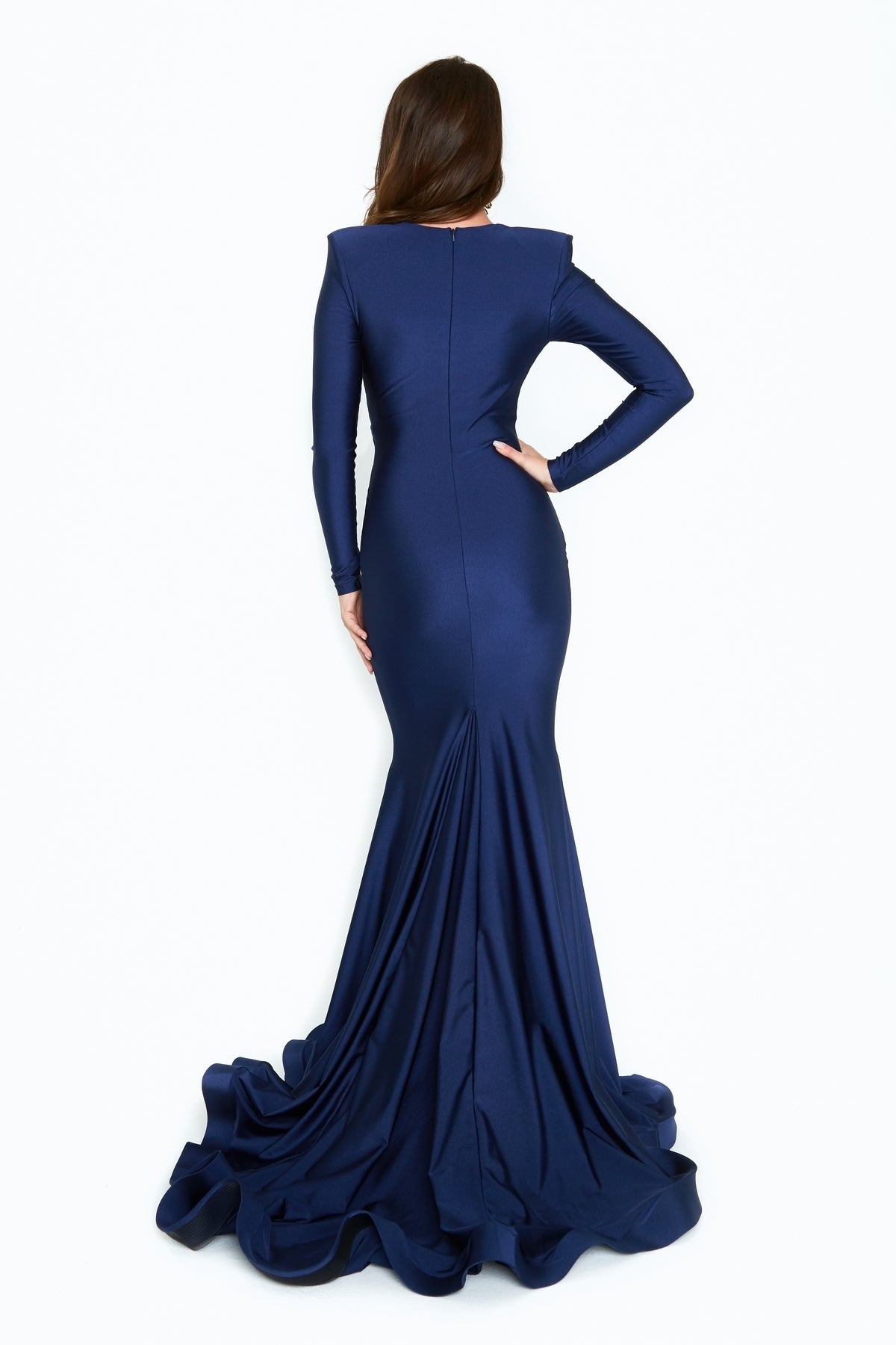 A woman faces away, wearing the navy blue Long-Sleeve Long V-Neck Prom Dress 6535H, featuring a fitted silhouette and flared floor-length train, set against a plain white background.